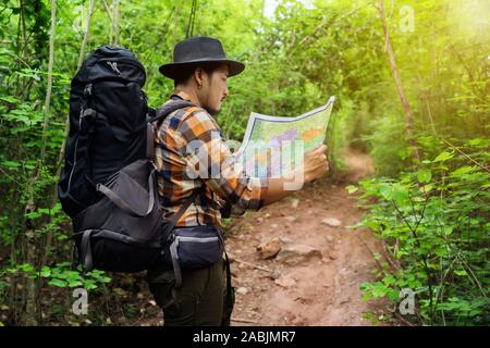 man traveler with backpack and map searching directions in the natural forest Stock Photo