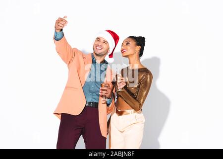 happy man in santa hat talking selfie with cheerful african american girl on white Stock Photo