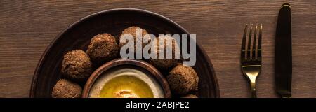 top view of falafel balls with hummus on plate near cutlery on wooden table, panoramic shot Stock Photo