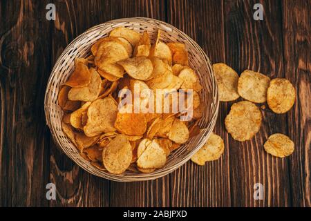 top view of delicious crispy potato chips in wicker basket on wooden table Stock Photo