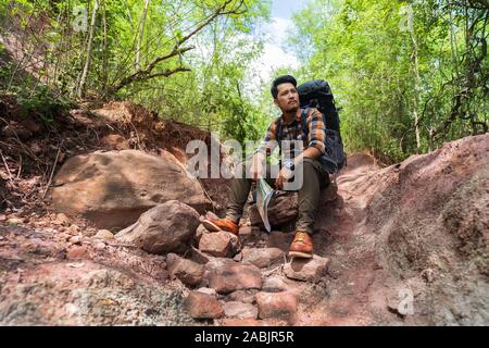 tired man traveler with backpack sitting and resting in the natural forest Stock Photo