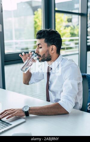 thirsty businessman drinking water while using laptop Stock Photo
