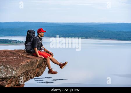 man traveler with backpack sitting on the edge of cliff, on a top of the rock mountain Stock Photo