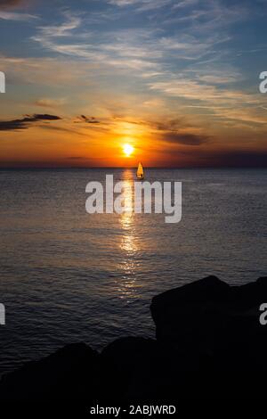 Lonely Wind surfer setting sail towards the dramatic and magnificent scenic sunset at the coast of the mediterranean sea in Trieste, Italy Stock Photo