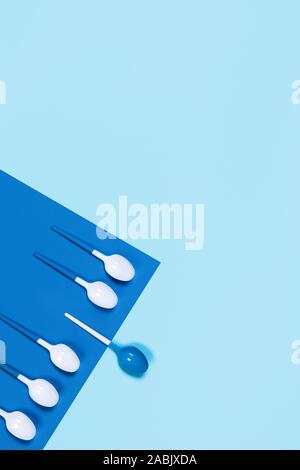 Concept of blue-white plastic spoons on two-toned blue background. Corner composition. Flat lay, top view, copy space. Stock Photo