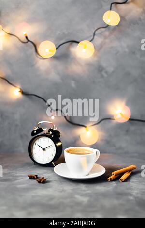 Christmas and New year composition with cup of coffee surrounded by cinnamon, lights and cloves on gray table. Stock Photo