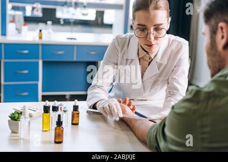 selective focus of attractive allergist holding ruler near hand on man in clinic Stock Photo