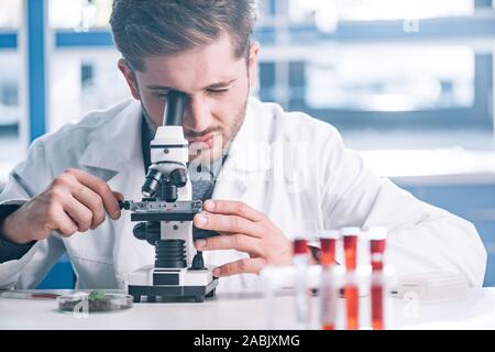 selective focus of bearded biochemist looking through microscope in laboratory Stock Photo