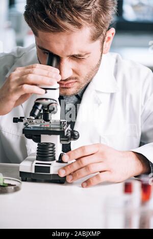 selective focus of handsome biochemist looking through microscope in laboratory Stock Photo