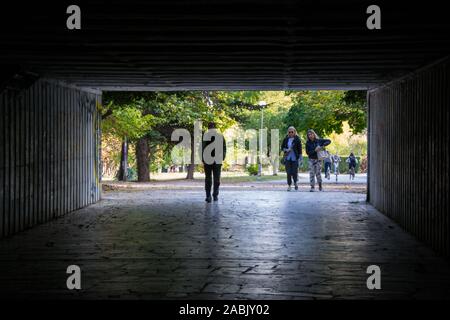 Varna, Bulgaria - People walking through a dark underpass with glowing end, underground passage, blurred people silhouettes