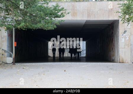 People walking through a dark underpass with glowing end, underground passage, blurred people silhouettes
