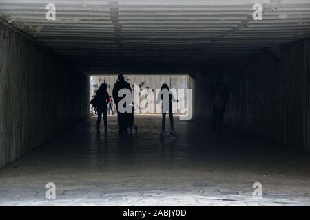 People walking through a dark underpass with glowing end, underground passage, blurred people silhouettes