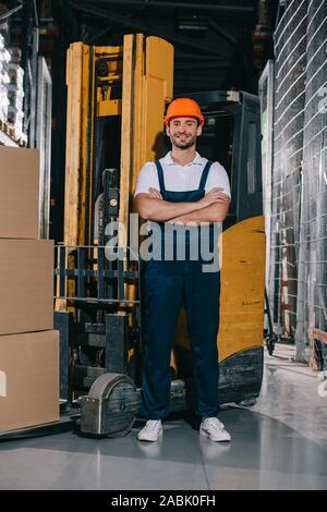 Worker near forklift truck with cardboard boxes in warehouse. Logistics ...