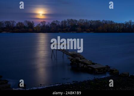 Real full moon over the autumn forest close to Dnieper river in Kiev, Ukraine. Soft clouds in the dark sky cover partially our natural satellite. A po Stock Photo