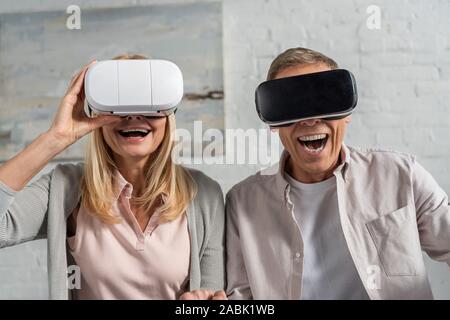 Laughing couple in virtual reality headsets at home Stock Photo