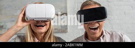 Panoramic shot of laughing couple in virtual reality headsets at home Stock Photo