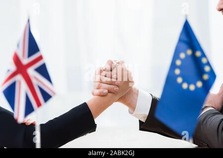 cropped view of ambassadors holding hands near european union and united kingdom flags