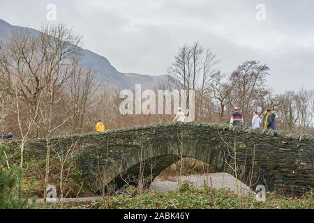 Ramblers cross the dry stone bridge over the river Derwent at the village of Grange in the Borrowdale valley, Lake district, Cumbria, England, on a ra Stock Photo