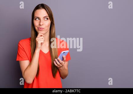 Portrait of positive cunning girl addicted social media user type sms on her cell phone think plans touch chin look copyspace wear red t-shirt Stock Photo