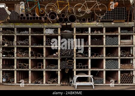 Different styles and sizes of old recycled metal pipes and profiles, construction materials laying on a shelf rack in a storage. Recycled metail piece Stock Photo
