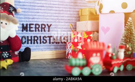 text MERRY CHRISTMAS on letter board on table, decorated with christmas ornament , gift box present and Santa Claus doll. selective focus Stock Photo
