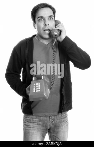 Thoughtful young Persian man standing and talking on old telephone while looking shocked Stock Photo