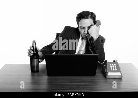 Persian businessman looking drunk while holding bottle of beer and old telephone with laptop on wooden table Stock Photo