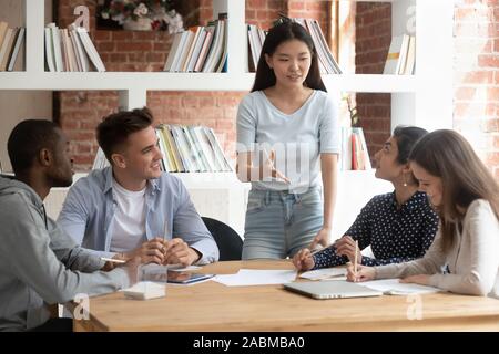 Smiling asian female team leader holding meeting with diverse groupmates. Stock Photo