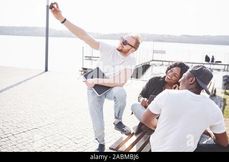 Beautiful multi ethnic friends using a laptop in the Street and make selphie. Youth lifestyle concept Stock Photo