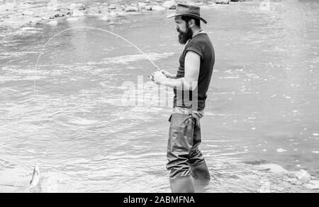 Fun of fishing is catching. Fishing masculine hobby. Brutal man wear rubber  boots stand in river water. Fisher weekend activity. Fisher with fishing  equipment. Fish on hook. Leisure in wild nature Stock