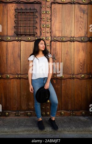 young Hispanic woman standing at an old colonial door Stock Photo