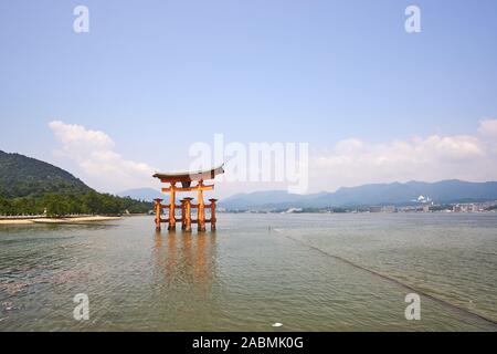 The vermilion torii shrine gate at Itsukushima Jinja Shrine on Miyajima stands in the water at high tide with mountains in the background Stock Photo