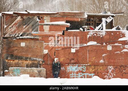 A redheaded, caucasian woman leans against the wall of an abandoned, snow-covered building in Provo Canyon, Utah, USA, near Bridal Veil Falls. Stock Photo