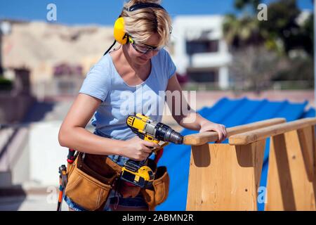 Handy woman with toolsbelt and yellow drill in her hands outdoors Stock Photo