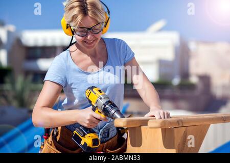 Handy woman with toolsbelt and yellow drill in her hands outdoors Stock Photo