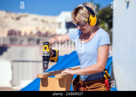 Handy woman with toolsbelt and yellow drill in her hands outdoors Stock Photo