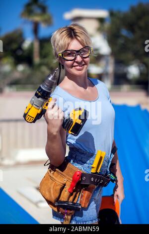 Handy woman with toolsbelt and yellow drill in her hands outdoors Stock Photo