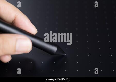 Close up hand holding a graphic tablet stylus writing on the graphic tablet  for illustrators and designers. Graphic design instrument. Selective focu Stock Photo