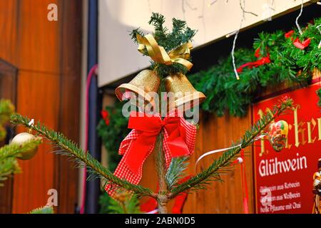 Heidelberg, Germany - November 2019: Two golden bells and red ribbon tied around pine tree as part of decoration on traditional Christmas market Stock Photo