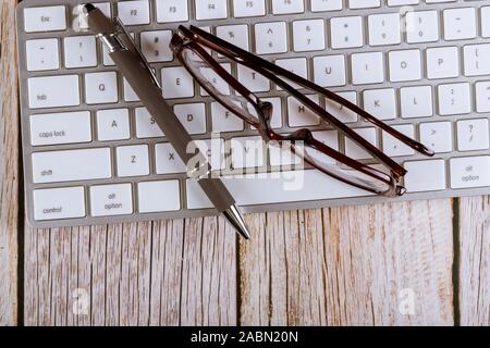 Workplace office desk of reading glasses and pen on the computer keyboard Stock Photo