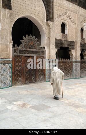 Old Moroccan Man in Traditional Clothing Walks with Walking Stick Across the Courtyard of Bou Inania Medersa (1350-56) Fez Morocco Stock Photo