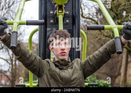 A young man in winter clothing works out on outdoor exercise equipment on a cold winters day. Perhaps showing his dedication to personal development. Stock Photo