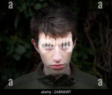 A young man in his late teens or early twenties looks menacing as he stares toward the camera with an intimidating gaze. Stock Photo