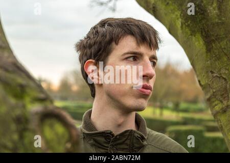 A young man standing among trees looks out with an air of sadness. Stock Photo