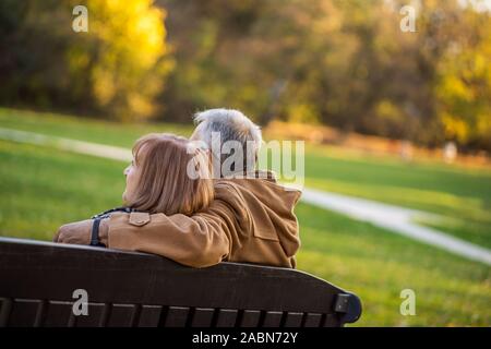 Romantic senior couple is sitting on bench in park and enjoying autumn. Stock Photo