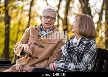 Senior couple is sitting on bench in park and enjoying autumn. Stock Photo