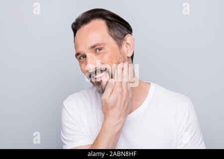 Photo of handsome positive mature man looking mirror toothy smiling hand checking silky skin after using shaving gel wear white t-shirt isolated grey Stock Photo