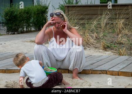 While the child is playing, the mother is talking on the cell phone. Stock Photo