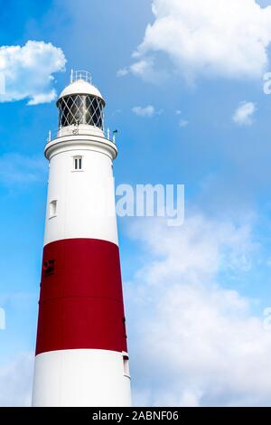 Tranquil scene of a large white and red lighthouse on a clear blue sky day surrounded by white clouds in England Stock Photo