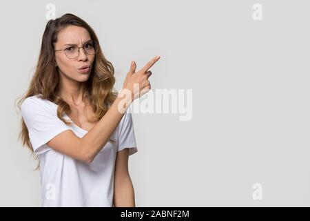 Doubting young woman wearing glasses pointing finger at copy space Stock Photo